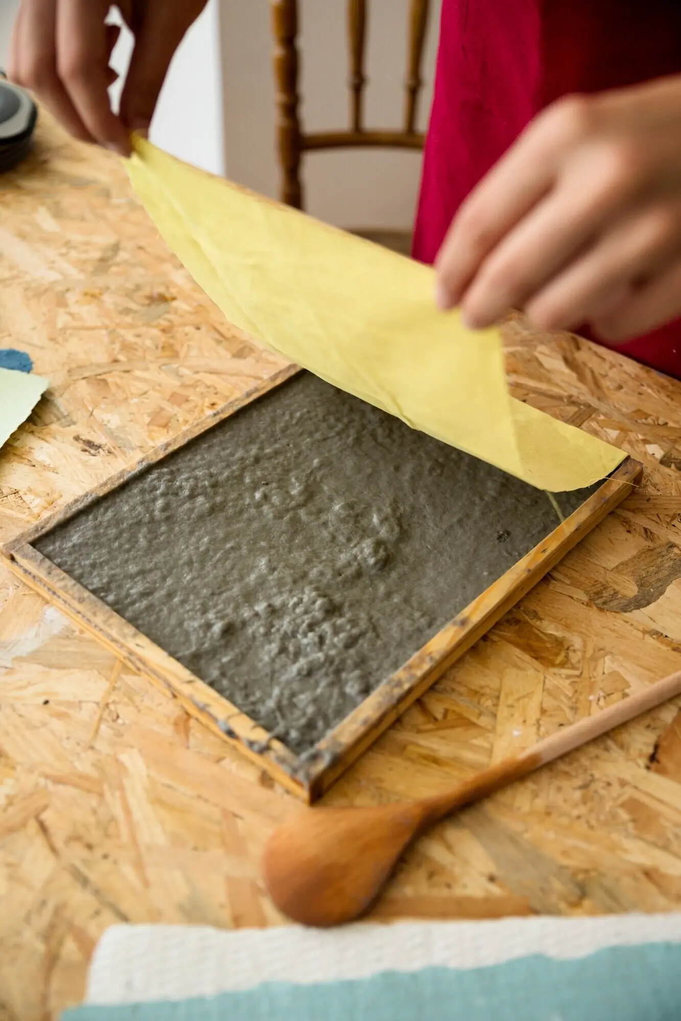 A woman's hand placing a yellow cloth over paper pulp on a wooden desk.